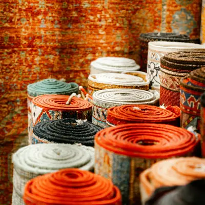 Aufgerollte Teppiche in Orange und Grau vor einem gemusterten Teppich